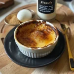 A close-up side view of a creamy crème brûlée protéinée in a ramekin, showcasing its golden caramelized top.
