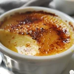 A close-up side view of a creamy vanilla crème brûlée with a caramelized sugar top.