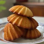 Golden-brown madeleines stacked on a plate, showcasing their shell shape.