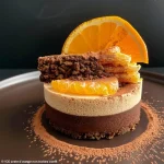 ['Close-up view of a rich chocolate mousse topped with orange zest.', 'Side view of a decadent chocolate mousse enhanced with orange flavor.', 'Creamy chocolate mousse garnished with bright orange zest and confit.', 'Luxurious chocolate mousse served in a glass, featuring an orange zest topping.']