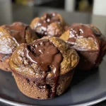 ['Close-up of a chocolate banana muffin with a moist texture.', 'Side view of a muffin featuring banana and chocolate chunks.', 'Juicy muffin topped with melted chocolate chips and banana slices.', 'Muffin showcasing a rich chocolate and peanut butter combination.']