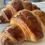 A close-up side view of golden croissants on a wooden surface.