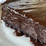 Close-up view of glossy black chocolate mirror glaze on a dessert.