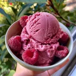Close-up of a vibrant pink raspberry sorbet in a clear bowl, showing a creamy texture.
