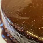 Close-up side view of glossy chocolate mirror glaze on a dessert.